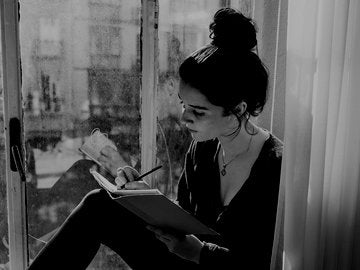 Young woman writing in notebook sitting in window